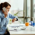 Frustrated businesswoman on a phone call, glancing at her watch while sitting at her desk.